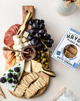 Wooden charcuterie board with assorted foods including cheese, fruits, and a box of Hayden Flour Mills white sonora crackers.