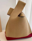 A knitted knot bag, featuring a khaki body and a contrasting red base, displayed on a white surface next to a book.