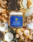 Momofuku Savory seasoned salt jar surrounded by mushrooms, garlic, and other ingredients on a wooden board.
