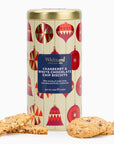 A cylindrical tin of Whittard of Chelsea Cranberry & White Chocolate Chip Biscuits on a white background, with several biscuits placed in front of the tin.