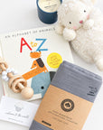 baby boy gift box contents: plush lamb, alphabet book, wooden rattle, gray organic cotton swaddle, and soy candle flat lay