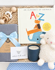 Baby boy gift box with plush white lamb, gray organic cotton swaddle, wooden teething rattle, A to Z alphabet book, and soy candle