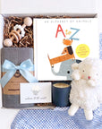 Baby boy gift box with plush white lamb, gray organic cotton swaddle, wooden teething rattle, A to Z alphabet book, and soy candle