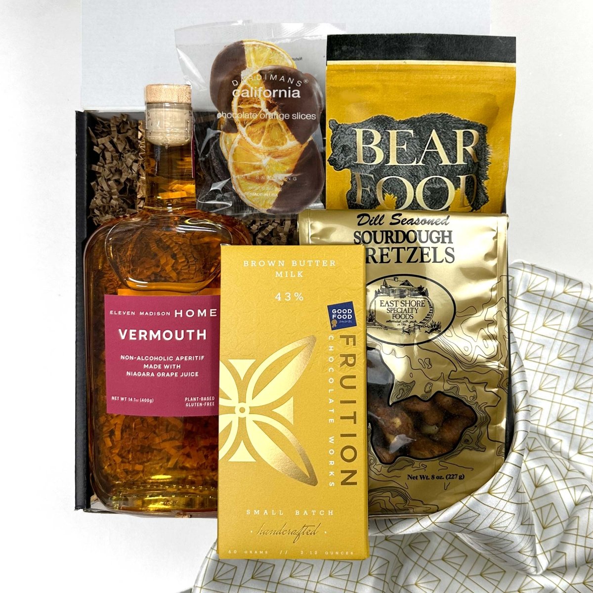 kadoo cocktail holiiday curated gift box with eleven madison home vermouth, fruition brown butter milk chocolate, pretzel, bear food peanut, chocolate orange slice and more,