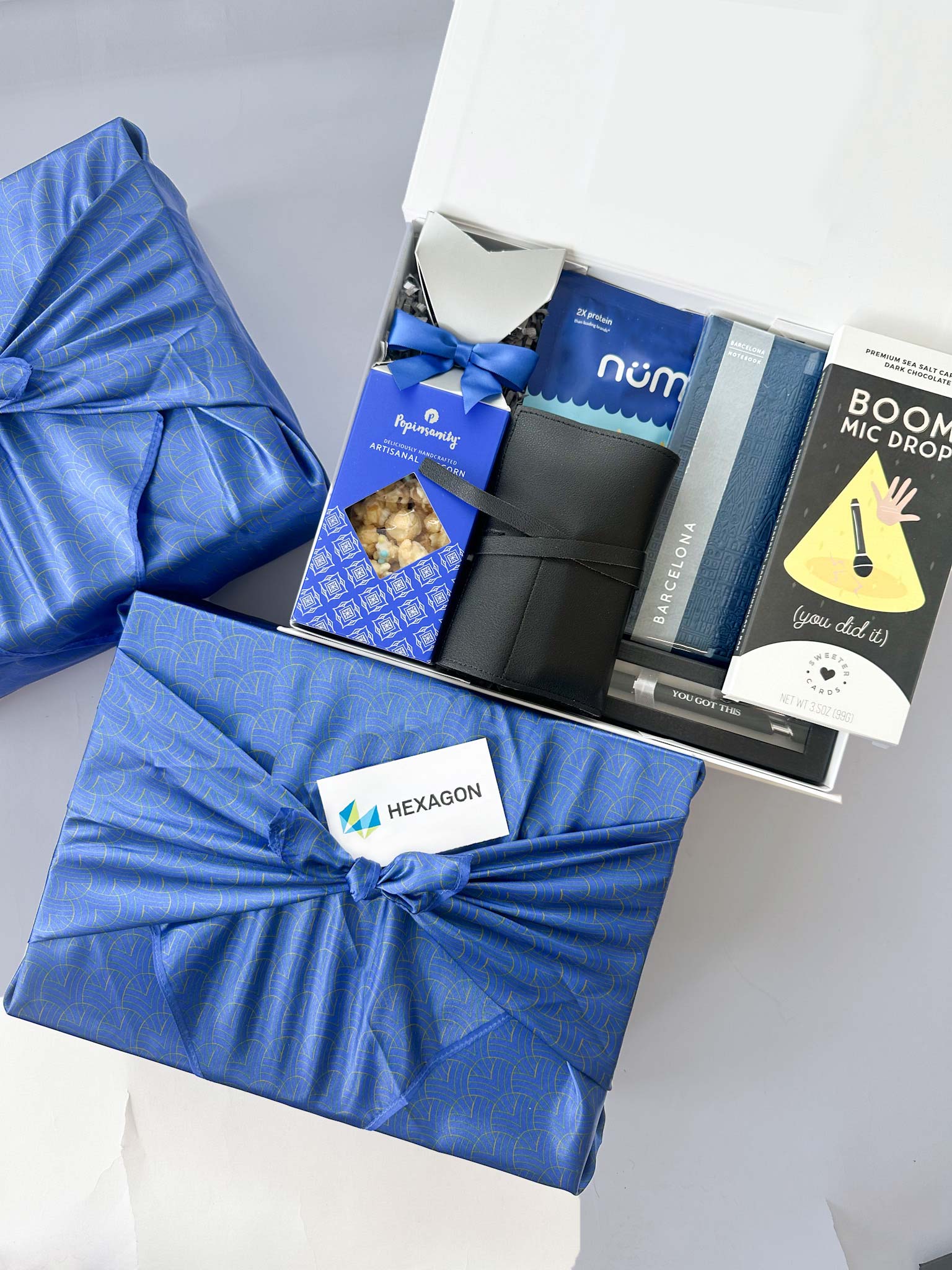 kadoo corporate gift box for Hexagon, wrapped in blue fabric wrap. Inside gifts popcorn, chocolate, notebook, pen, cable organizer and more.
