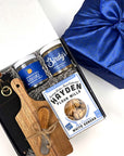 Gift set with momofuku's seasoned slat, Birdy's seasoning jars, a wooden cutting board, and a box of Hayden Flour Mills cracker, black apron, on a white background.