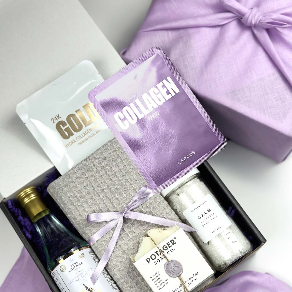 kadoo lavender lush spa gift box with lavender distilled water, soap, hand towel in gre, lapcos collagen and 24K gold foil, calm bath salt and more, wrapped in purple furoshiki fabric.