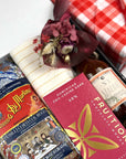 kadoo pasta night curated gift box in red fabric wrap with dry pasta, chocolate bar, homemade tomato sauce, yellow stripes kitchen towel, olive wooden fork utensil, and more. It has red dried flower bouquet.