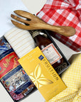 kadoo pasta night curated gift box in red fabric wrap with dry pasta, chocolate bar, homemade tomato sauce, yellow stripes kitchen towel, olive wooden fork utensil, and more. It has red dried flower bouquet.
