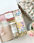 kadoo rose garden gift box for her in furoshiki fabric wrap. Gifts include: bath soak, relax bath salt, farmhouse biscuit, handmade soap, rose quartz facial roller and more.