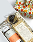 kadoo tea time curated gift wrapped in orange pattern fabric. Gift inside the box:  tea, natural raw honey, wooden honey dipper, dandelion chocolate bar, orange chocolate crisply slice and more.