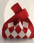 A red and white argyle knit gift bag with a loop handle, photographed on a clean white surface with a soft, minimalist background.
