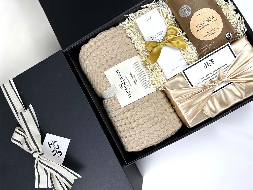 Gift box with a knitted blanket, wrapped items, and decorative ribbons on a white background