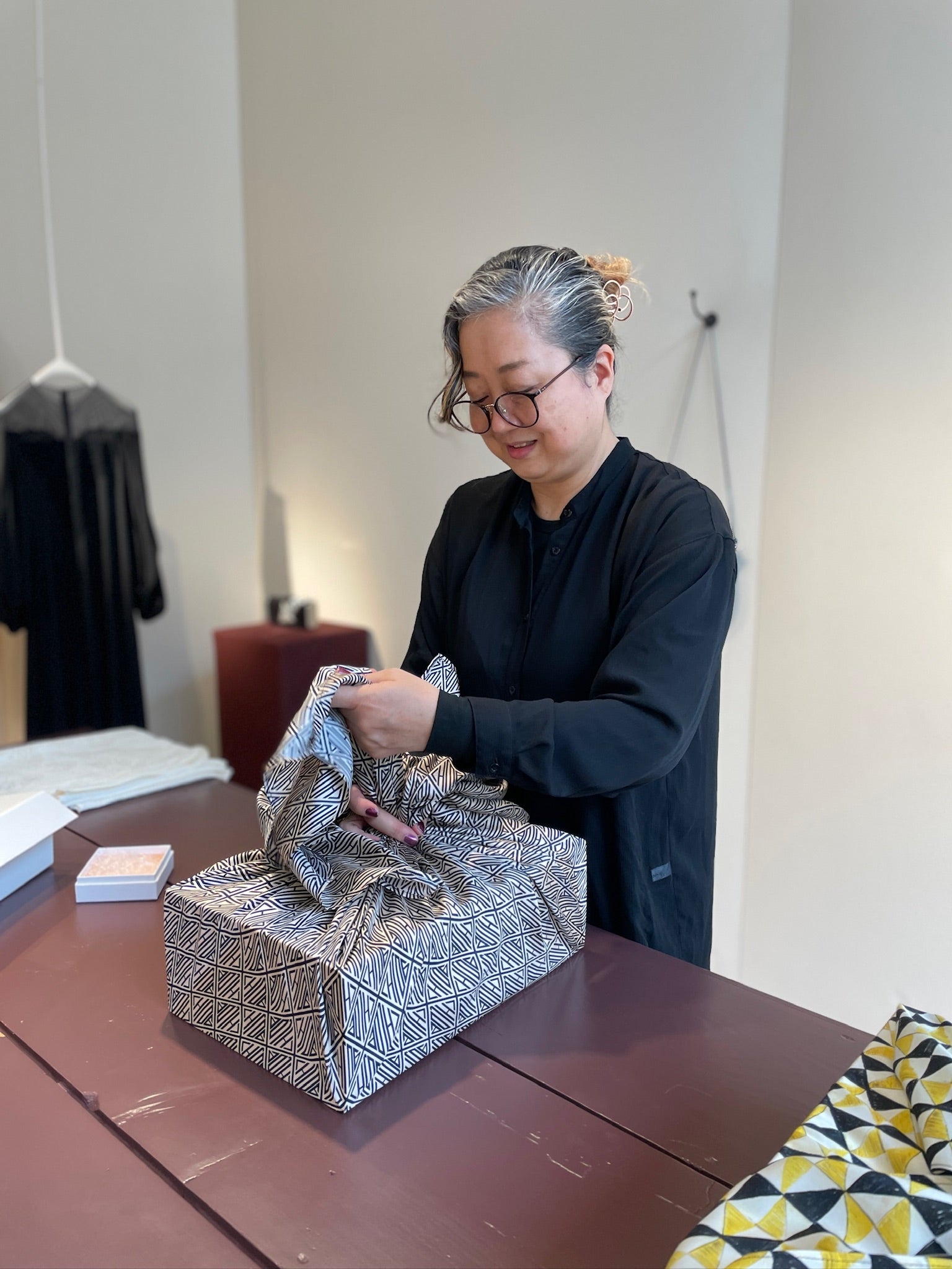 Person wrapping a gift with silver paper on a wooden table.