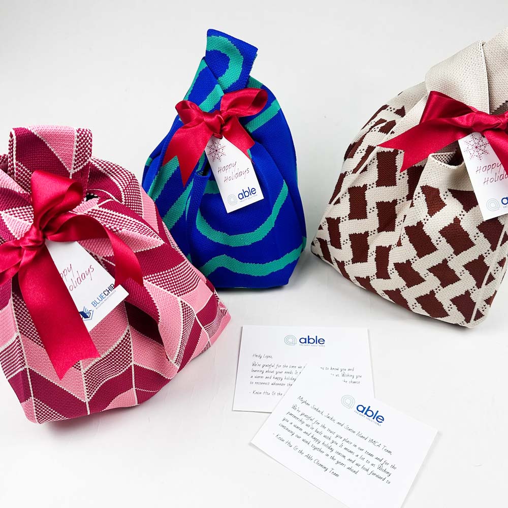 Three colorful gift bags with ribbons and Able branded tags on a white surface.