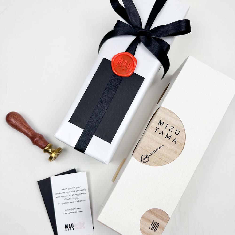 Gift wrapped in white paper with black ribbon and red wax seal, next to a wooden packaging with 'Mizu Tama' branding.