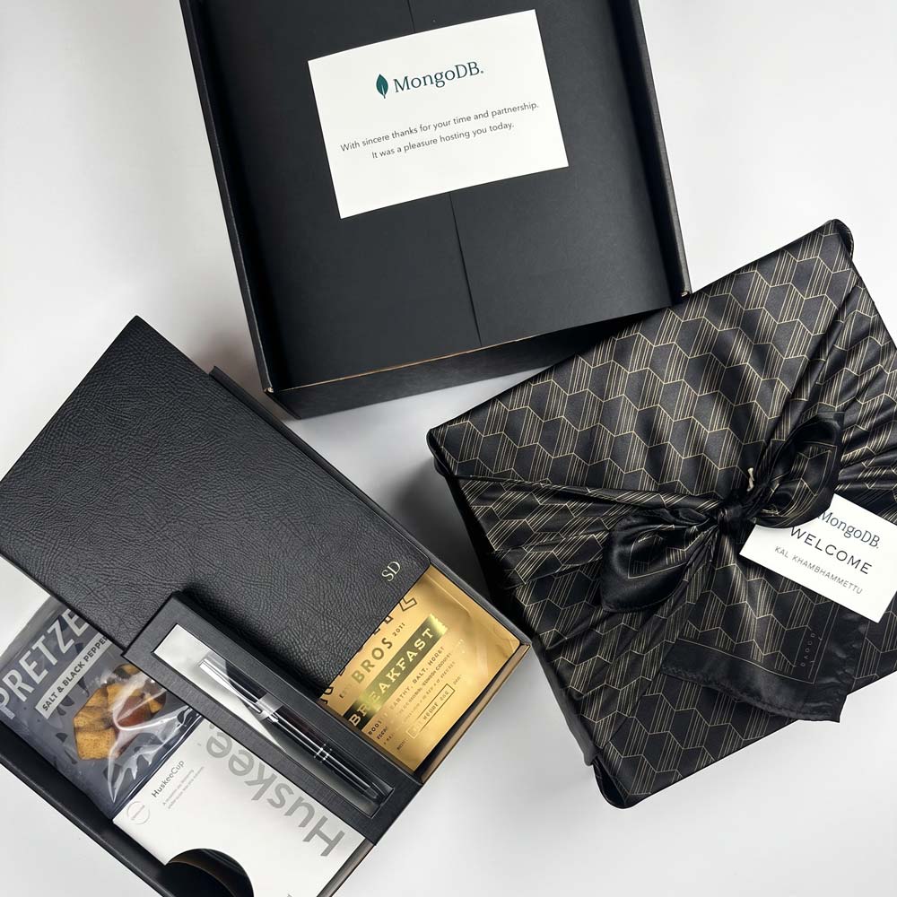 Gift set with a black box, gold card, and patterned black bag on a white background