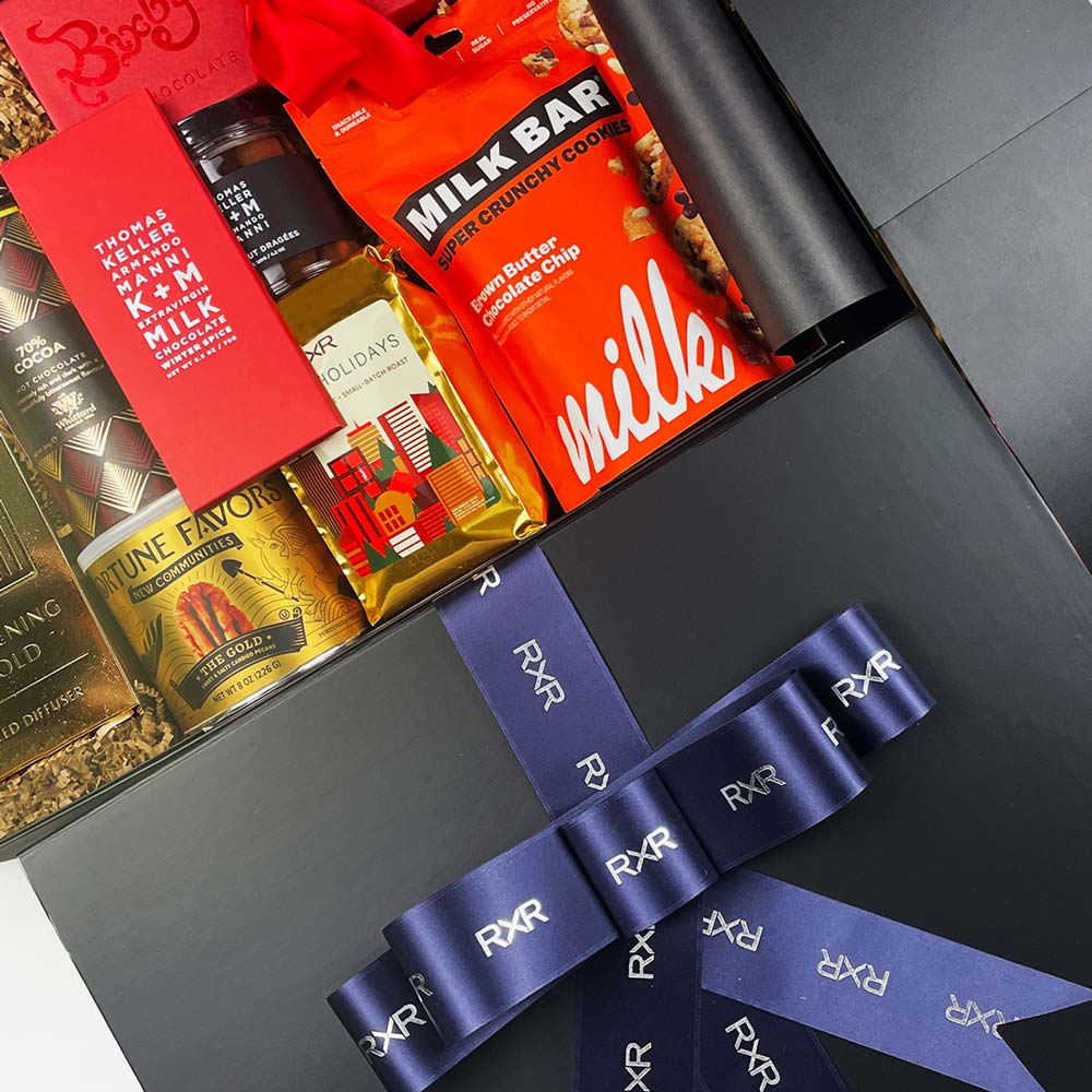 Assorted chocolate bars in a decorative box with a blue ribbon, featuring brands like Milk Bar and Godiva.