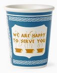A white ceramic coffee cup with a blue and white Greek key pattern and a central white shield containing the text 'WE ARE HAPPY TO SERVE YOU' in gold, above illustration of three gold coffee cups.