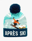 A knit pom-pom beanie with a dark navy blue top and cuff, featuring a light blue and white ski-themed graphic with a skier and the text 'APRÈS SKI' in white on the cuff.