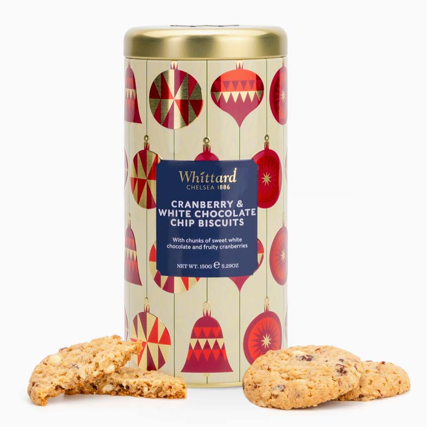 A cylindrical tin of Whittard of Chelsea Cranberry &amp; White Chocolate Chip Biscuits on a white background, with several biscuits placed in front of the tin.