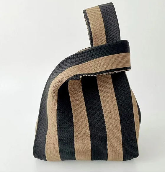 A knitted striped bag with alternating black and beige vertical stripes, featuring a wide top handle, shown against a plain white background