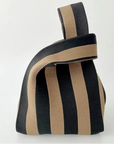A knitted striped bag with alternating black and beige vertical stripes, featuring a wide top handle, shown against a plain white background