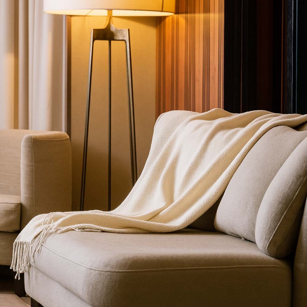 Beige blanket draped over a beige sofa with a lamp in the background