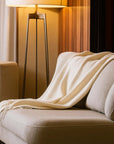 Beige blanket draped over a beige sofa with a lamp in the background