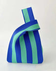 A small fabric handbag with bold vertical blue and mint green stripes, featuring a matching fabric loop handle, set against a plain light background.