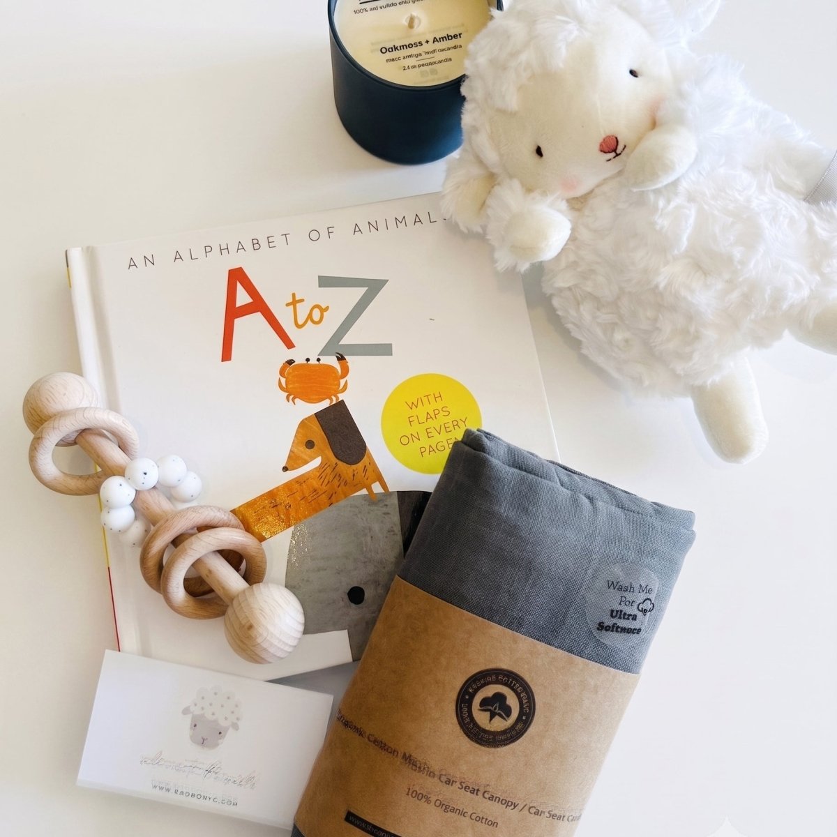 aby boy gift box contents: plush lamb, alphabet book, wooden rattle, gray organic cotton swaddle, and soy candle flat lay