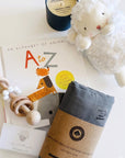 aby boy gift box contents: plush lamb, alphabet book, wooden rattle, gray organic cotton swaddle, and soy candle flat lay