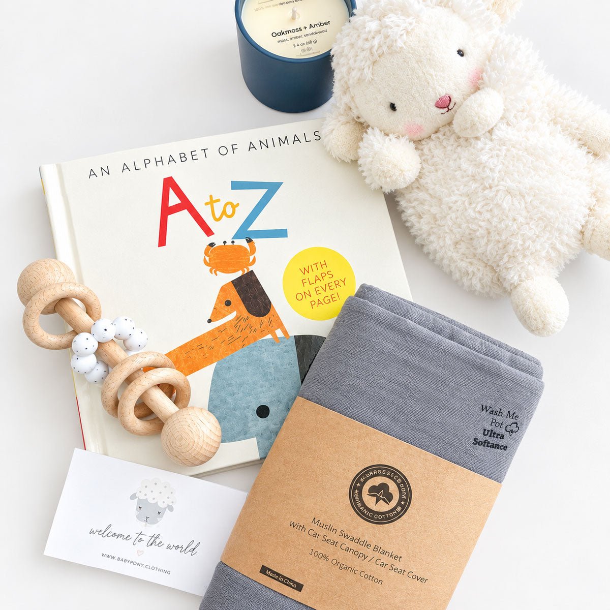 baby boy gift box contents: plush lamb, alphabet book, wooden rattle, gray organic cotton swaddle, and soy candle flat lay