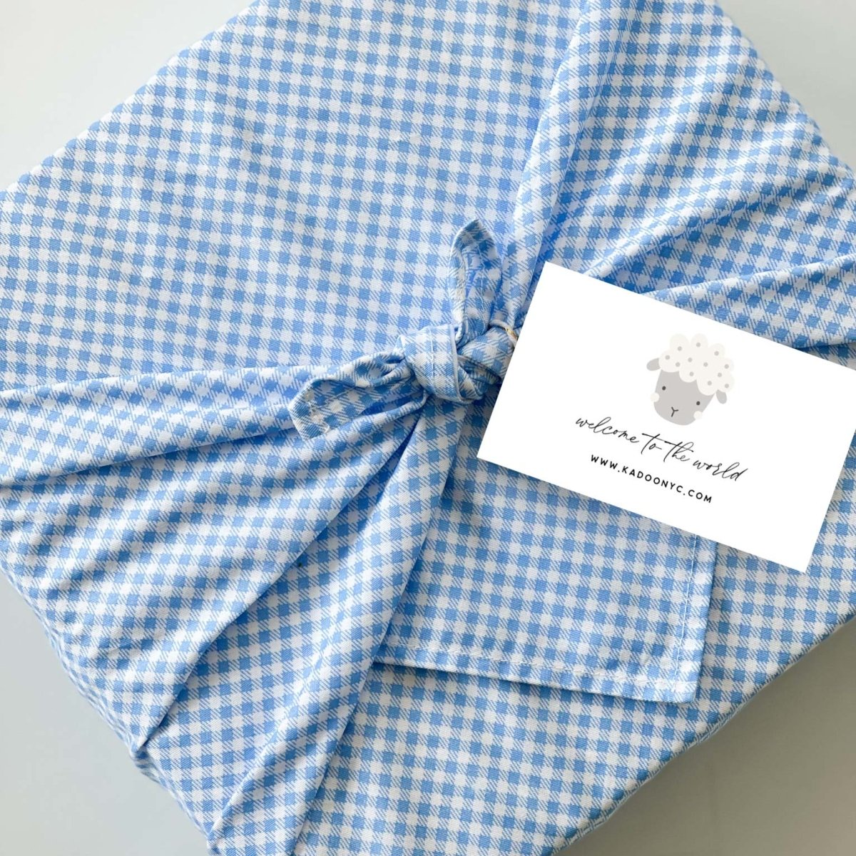 Baby boy gift box wrapped in blue gingham Furoshiki cotton fabric with welcome to the world lamb card