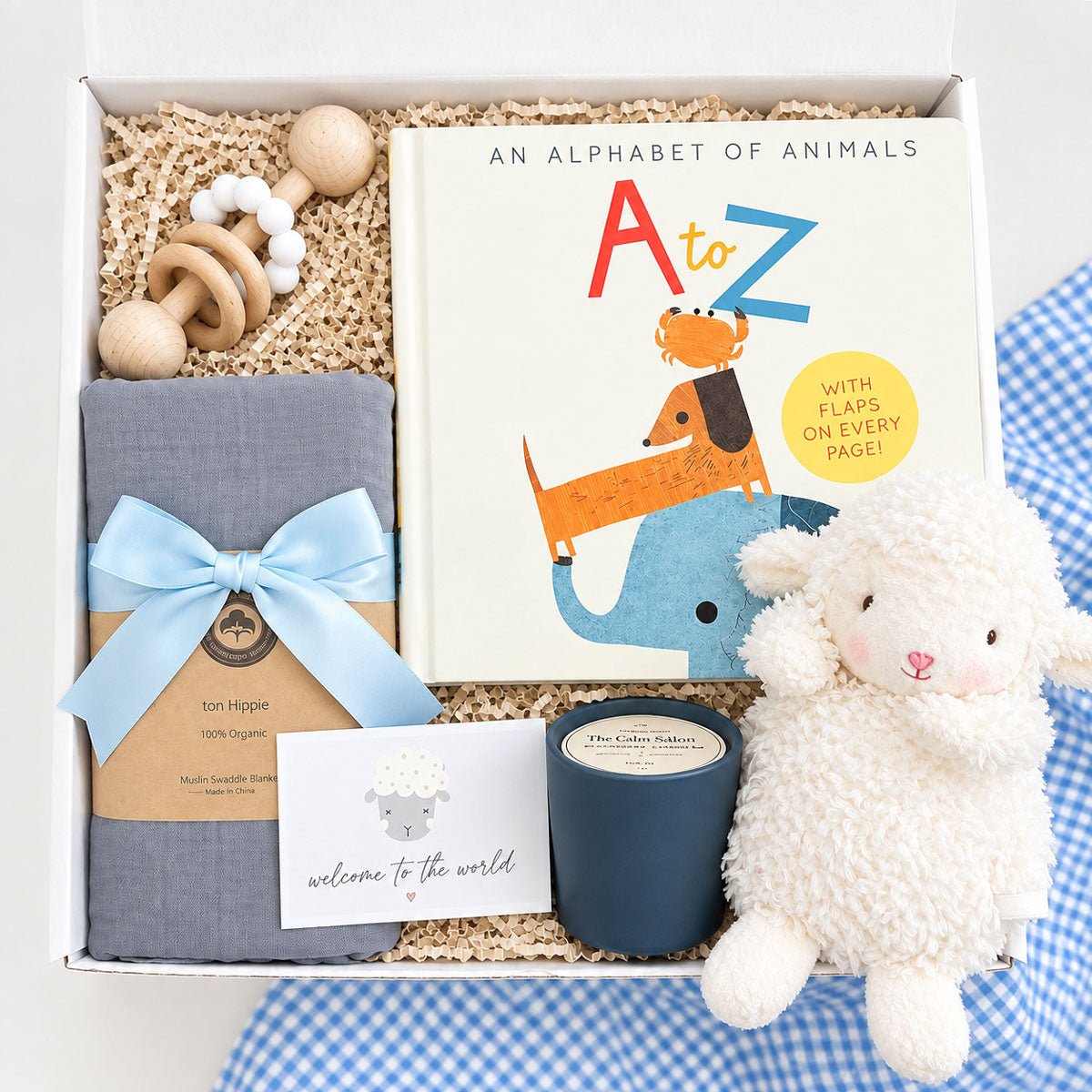 Baby boy gift box with plush white lamb, gray organic cotton swaddle, wooden teething rattle, A to Z alphabet book, and soy candle