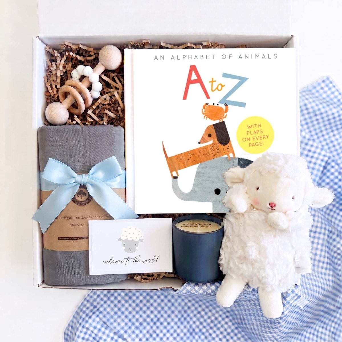 Baby boy gift box with plush white lamb, gray organic cotton swaddle, wooden teething rattle, A to Z alphabet book, and soy candle
