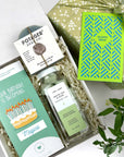 kadoo birthday celebration gift box. Inside gifts: birthday cake chocolate bar, soap eucalyptus mint, white tea aloe sugar scrub, happy birthday laser cut notecard in green and blue. Wrapped in green floral pattern gift box.