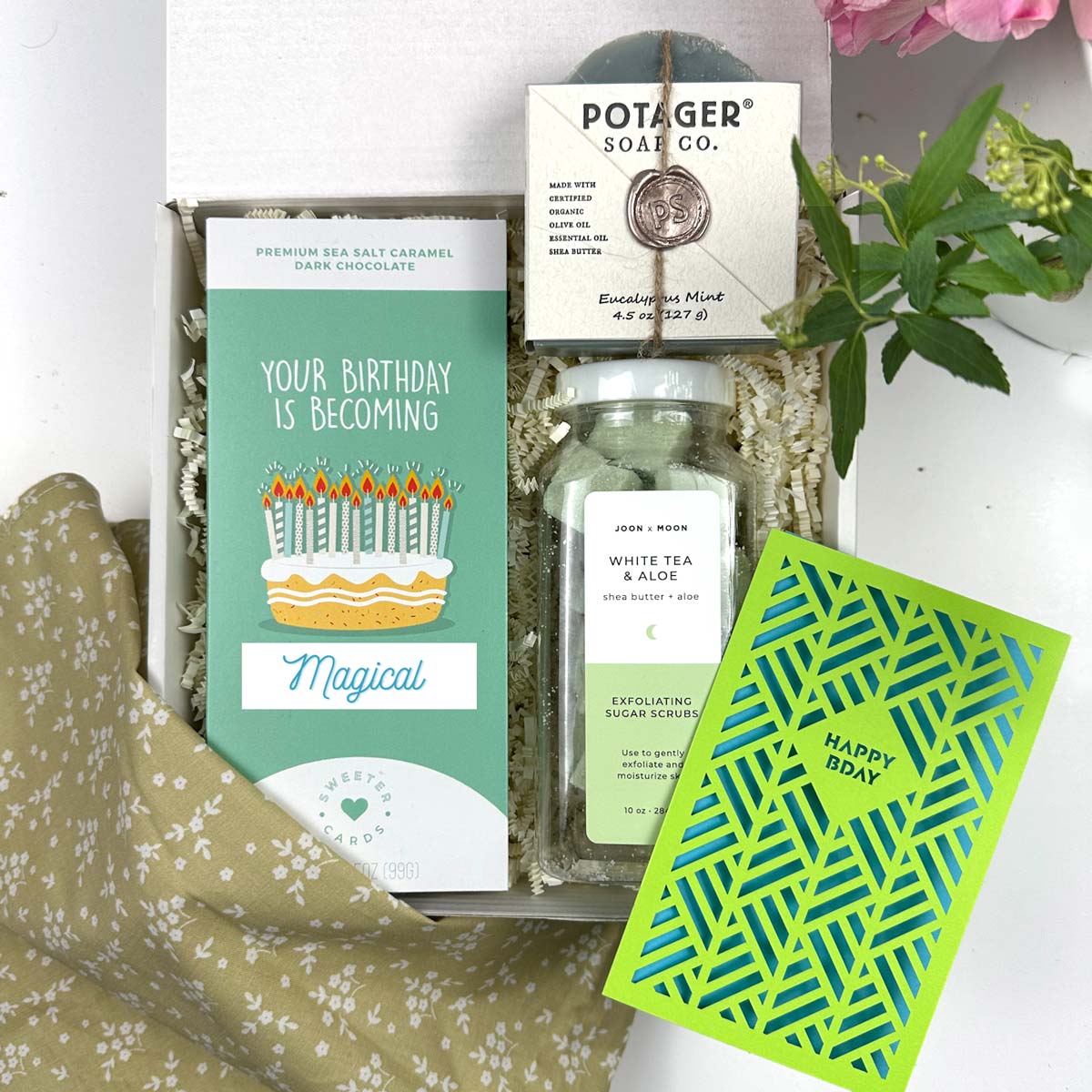 kadoo birthday celebration gift box. Inside gifts: birthday cake chocolate bar, potager soap eucalyptus mint, white tea aloe sugar scrub, happy birthday laser cut notecard in green and blue, green fabric with flowers pattern.