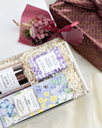 kadoo curated gift with milk chocolate chip in purple packaging, vanilla noir candle in glass pink container, lavender oatmeal bar soap, dried-flower and furoshiki fabric wrap