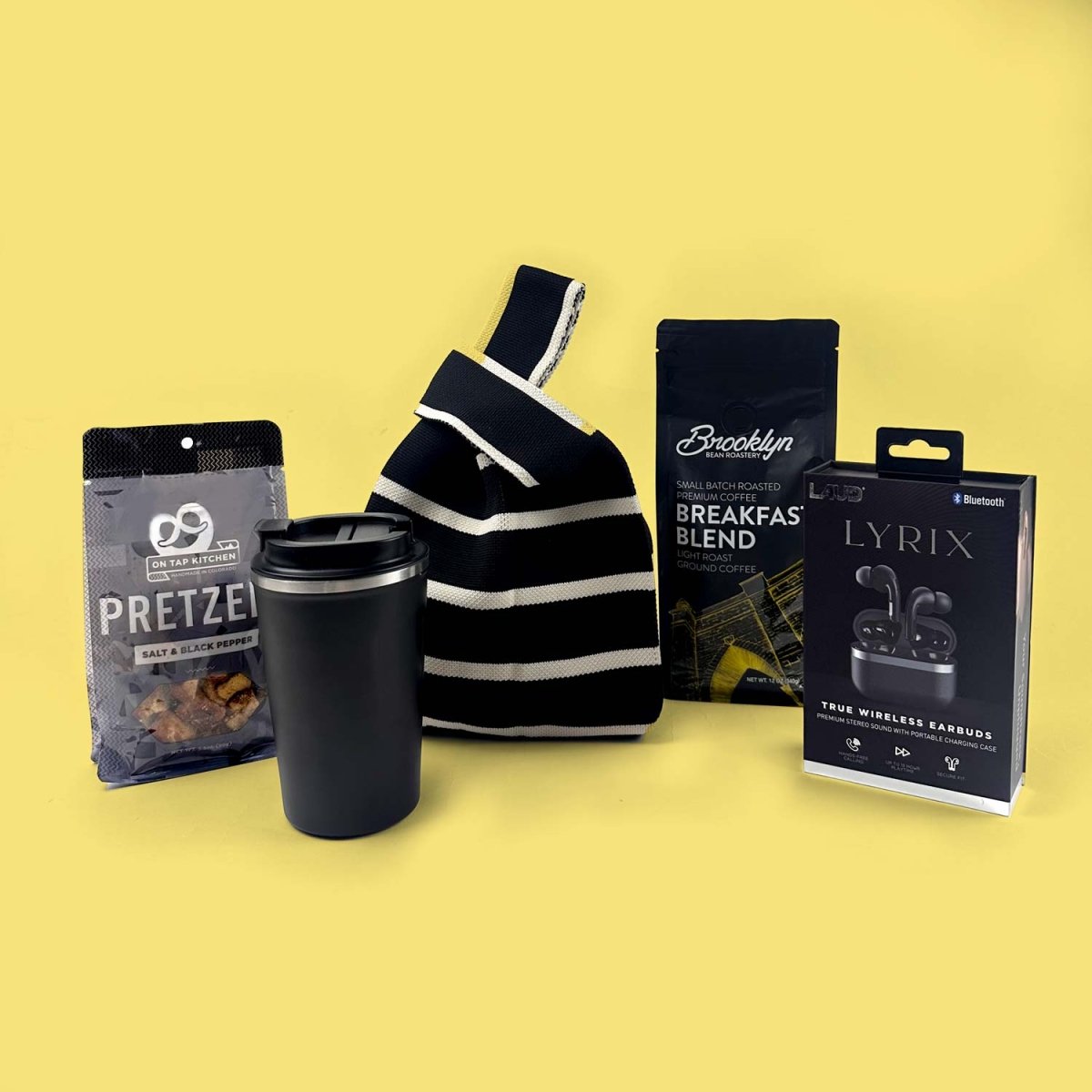 Black and white striped sling bag with a black tumbler, pretzel snack package, and electronic device packaging on a yellow background.