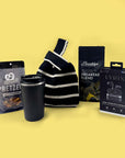 Black and white striped sling bag with a black tumbler, pretzel snack package, and electronic device packaging on a yellow background.