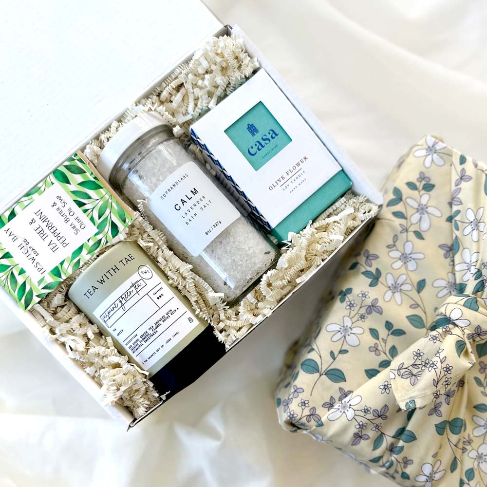 kadoo calm spa curated gift box wrapped in reusable furoshiki fabric wrap. gifts included lavender bath salt, olive flower soy candle, tea tree peppermint soap, jasmine tea and more