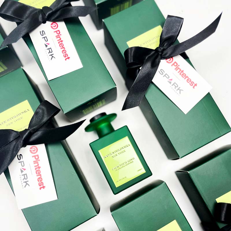Green perfume bottle with black ribbons and 'Pinterest Spark' labels on a white background