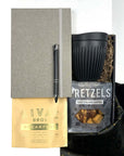 KADOO Desk essentials gift box with gray journal, black silver pen, breakfast tea, black mug, pretzels, in black gold fabric wrap and more.