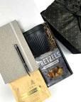 KADOO Desk essentials gift box with gray journal, black silver pen, breakfast tea, black mug, pretzels. Wrapped in black gold furoshiki style fabric wrap.