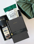 kadoo do great things gift box with black sol cup, shortbread, black notebook, pen, espresso beans chocolate and more. In Furoshiki fabric wrap.