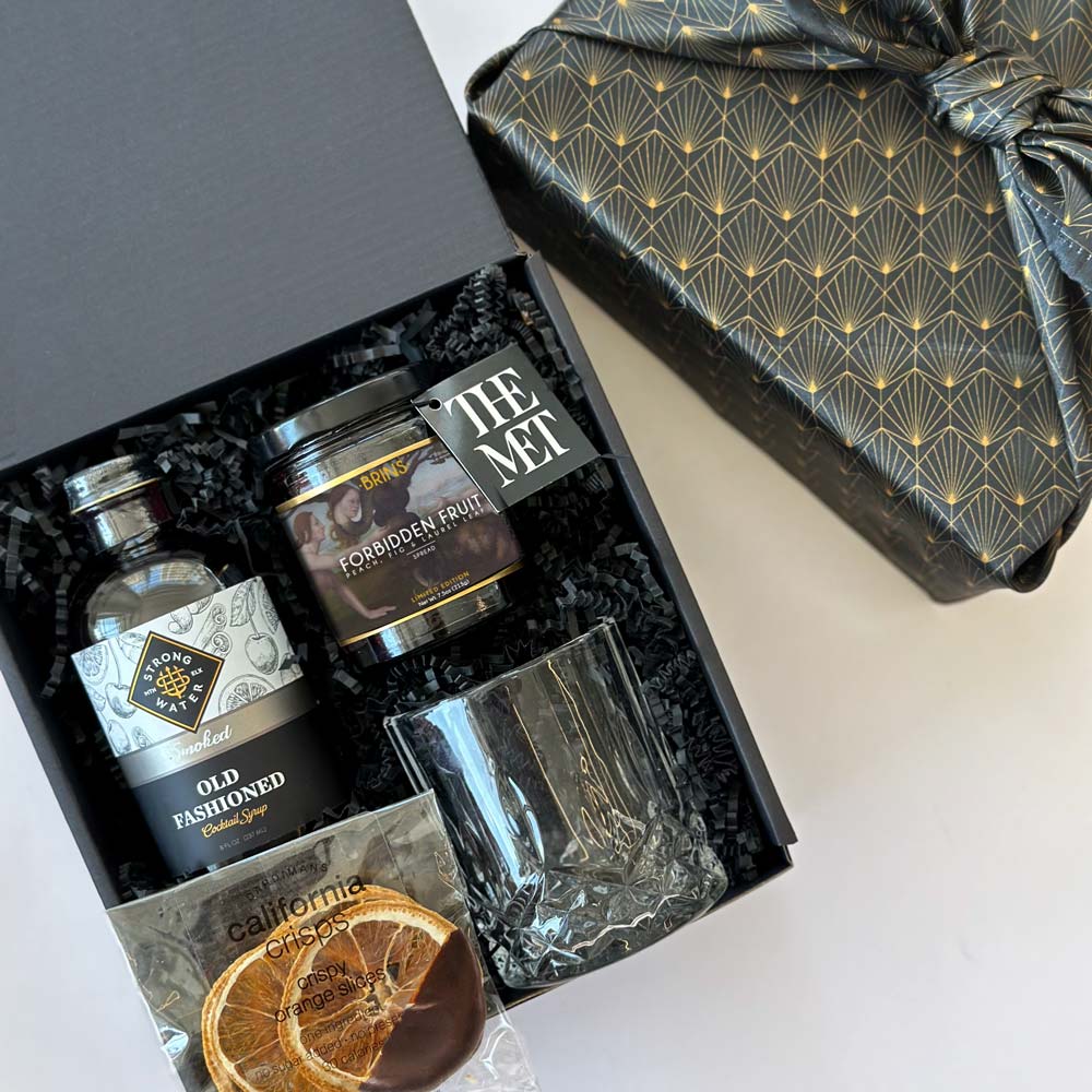 kadoo old fashioned curated gift box with cocktail syrup, The MET jam, viski crystal tumbler, orange slice and more. Wrapped in black reusable furoshiki fabric wrap. 