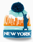 A knit New York beanie hat featuring a navy blue pom-pom, a light blue and orange city skyline graphic with the Statue of Liberty, and a navy blue cuff with 'NEW YORK' in white text.