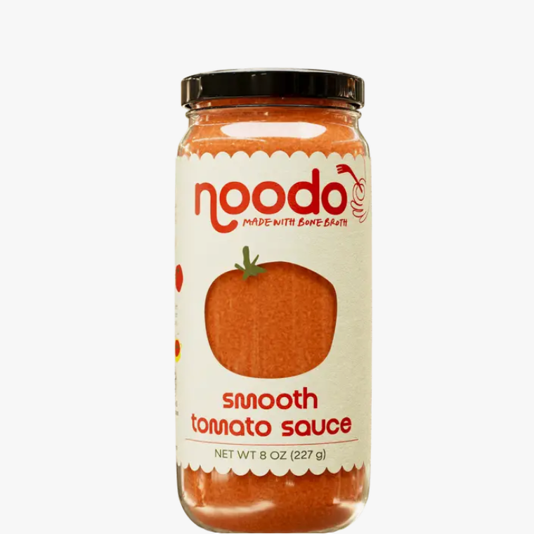 A glass jar of Noodo Smooth Tomato Sauce with a black lid and a cream-colored label featuring a tomato graphic, set against a white background.