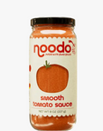 A glass jar of Noodo Smooth Tomato Sauce with a black lid and a cream-colored label featuring a tomato graphic, set against a white background.